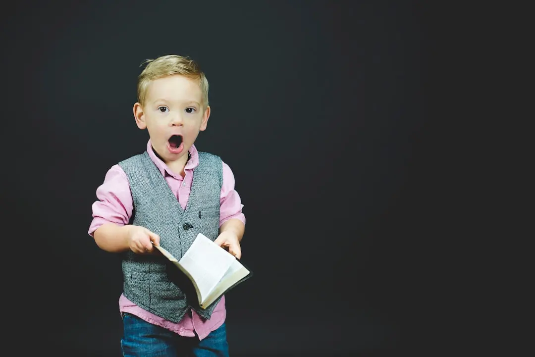 boy wearing gray vest and pink dress shirt holding book